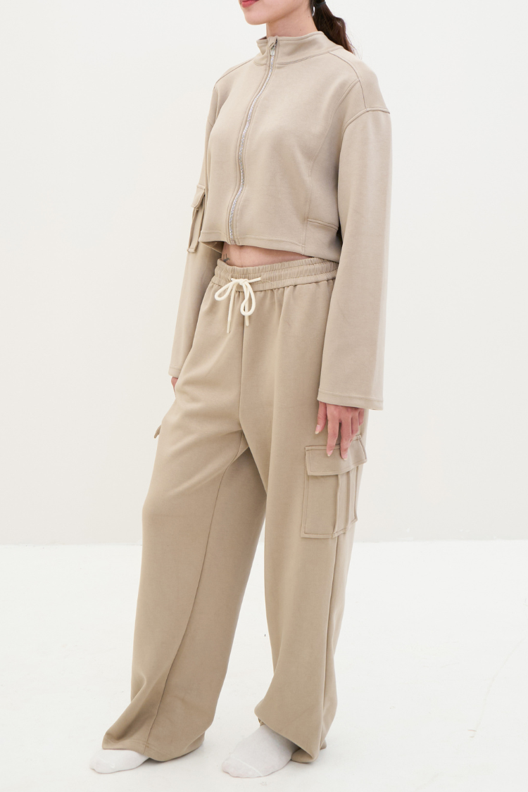 ELOWEN sports-set (Toffee) Track suit zipper sweater and sweatpants beige color. Active wear front display. Left side image. Person wearing a beige tracksuit on a white background.