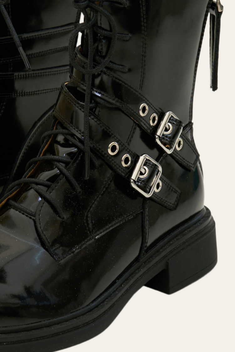 Black patent leather boot with buckles on a light gray background. Black high-top boots with zippers. Women’s Chelsea boots, timberland boots, military boots, heels boots, black boots with zippers. Leather boots. Close up side view image.