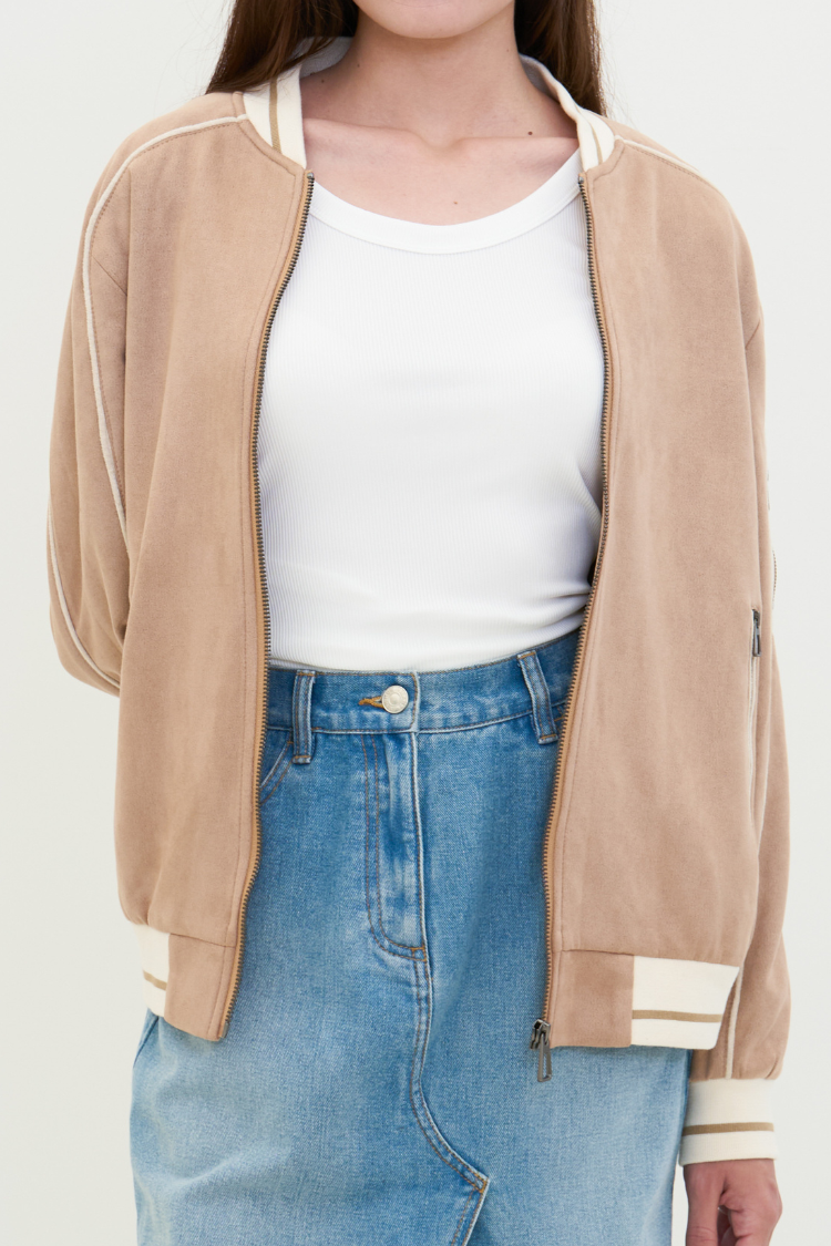 Person wearing a beige cardigan over a white tank top and blue jeans on a plain background. NAILA BASIC jacket in beige color with zipper. Unisex jacket. Close up image.