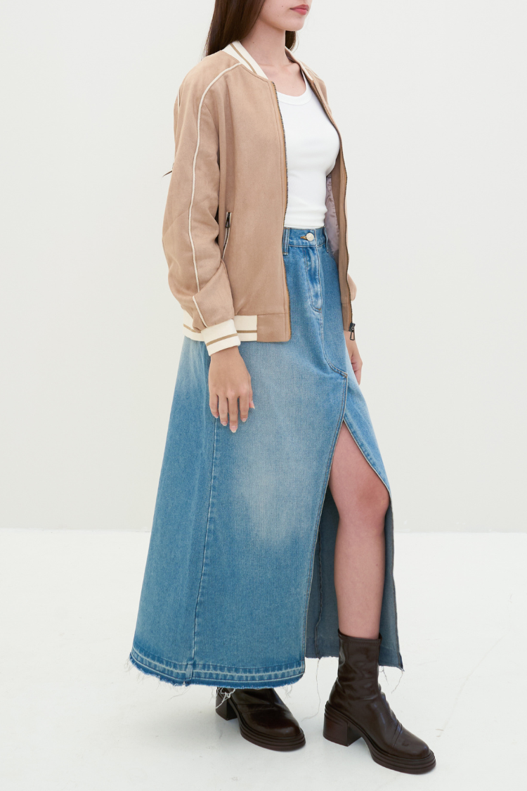 Person wearing a beige bomber jacket, white top, and blue denim skirt on a plain background. Person wearing a beige bomber jacket with white trim. NAILA BASIC jacket in beige color with zipper. Unisex jacket. Right side Image.