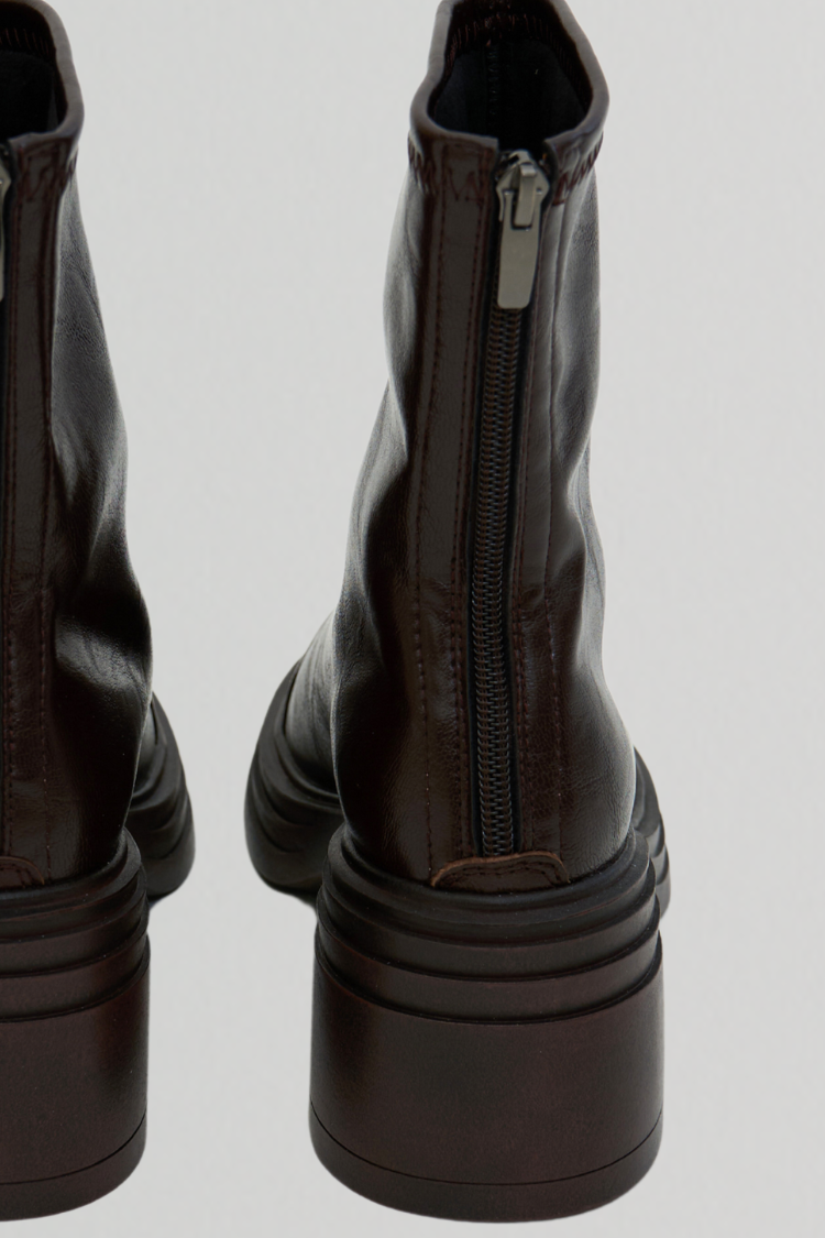 Pair of dark brown leather boots with zippers on a light gray background. Pair of women's black leather ankle boots. Chelsea boots. Timberland boots. Brown shoes. Brown boots. Riding boots. back close up image.