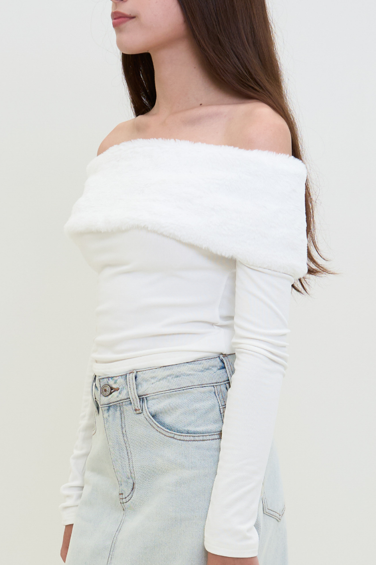 CAPUCINE top 2 - Women's white blouse with fur and wool side image. Woman wearing a white off-shoulder top and light blue jeans against a plain background. 