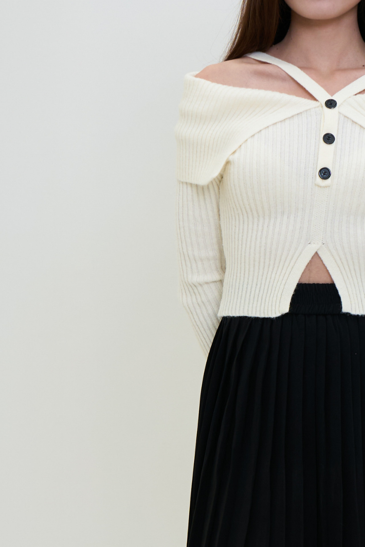 Woman wearing a cream-colored off-shoulder knit ribbed top with black buttons.  CELINENA top Front image. White ribbed sweater blouse with cut-out design front shoulder close up.