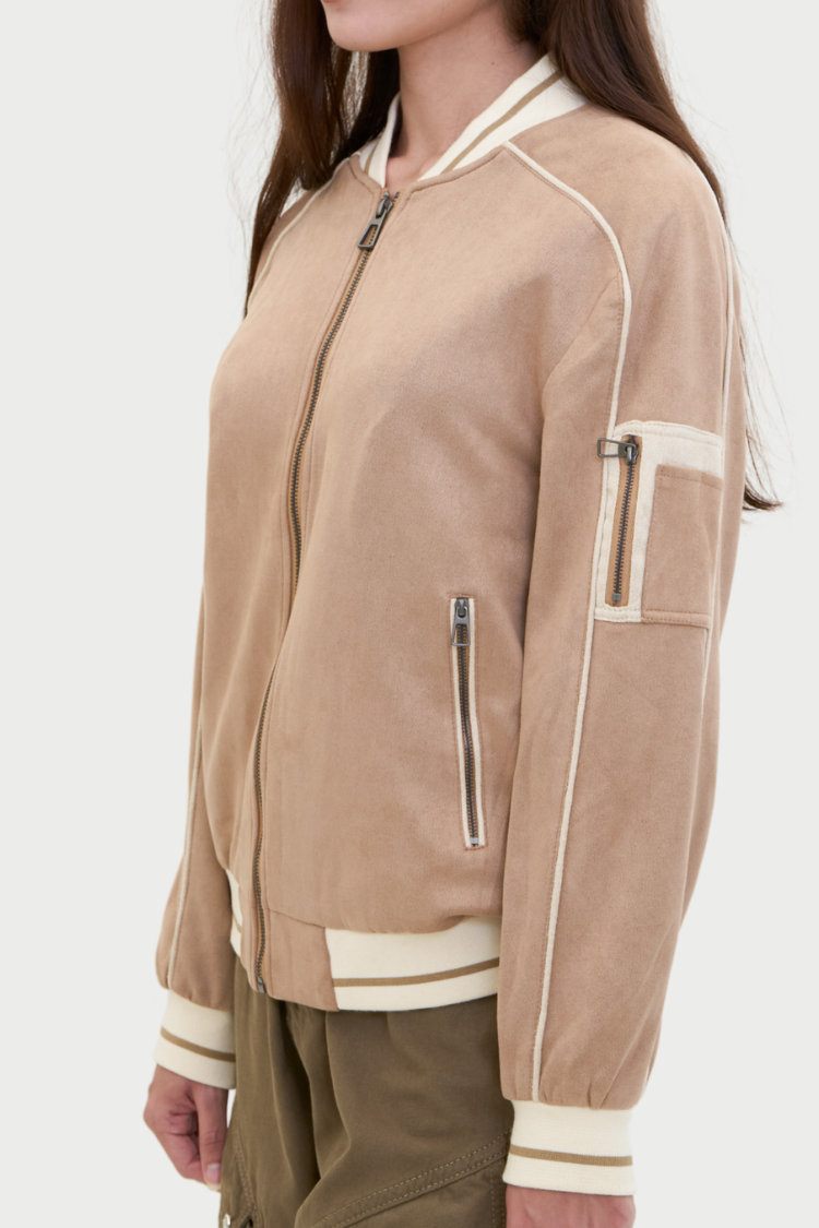 Beige bomber jacket with white accents worn by a women. Person wearing a beige bomber jacket with white trim. NAILA BASIC jacket in beige color with zipper. Unisex jacket. Side display. 