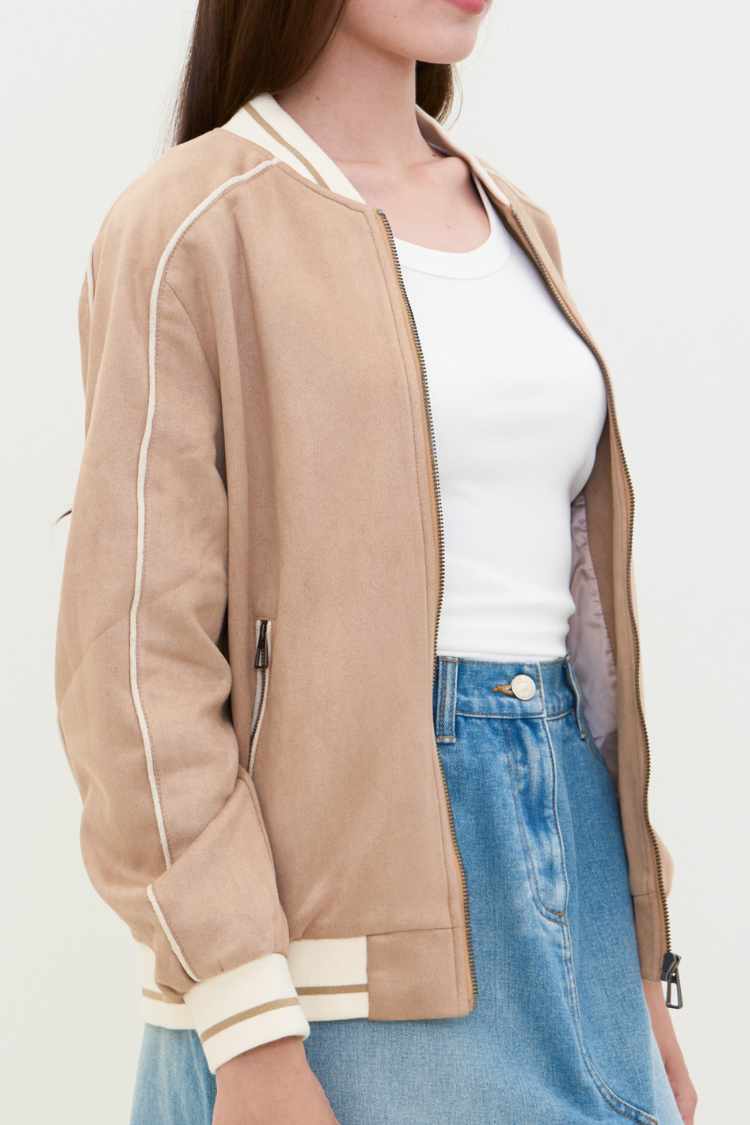 Person wearing a beige bomber jacket with white trim. NAILA BASIC jacket in beige color with zipper. Unisex jacket.